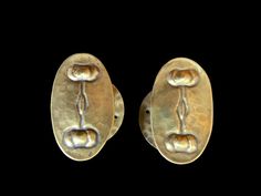 two gold earrings are shown against a black background and one is shaped like an oval