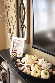 a black table topped with lots of white pumpkins and seashells in front of a flat screen tv