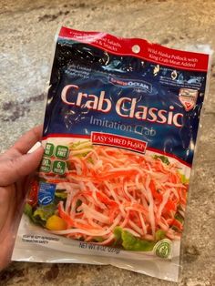 a hand holding a bag of crab salad in it's left side on the counter