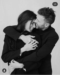 a man and woman hugging each other in front of a white wall with the words love written on it