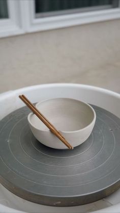 a white bowl with two chopsticks in it on top of a gray plate