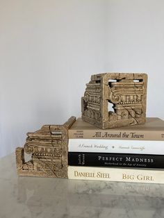 three books are stacked on top of each other in front of a white wall and marble table