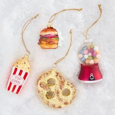 three ornaments are shown on the snow with candy, popcorn, and burgers in them