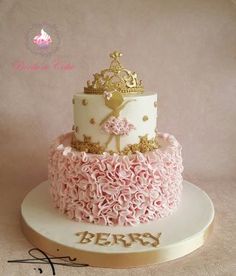 a three tiered cake decorated with pink and gold icing, topped with a crown