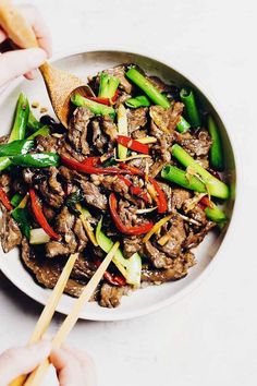 a white plate topped with meat and veggies next to wooden chopsticks