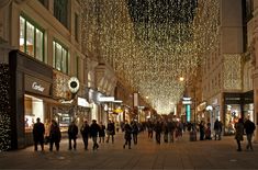 many people are walking down the street with christmas lights hanging from the buildings above them