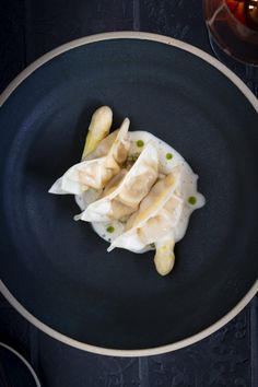 a black plate topped with dumplings and sauce on top of a blue table cloth