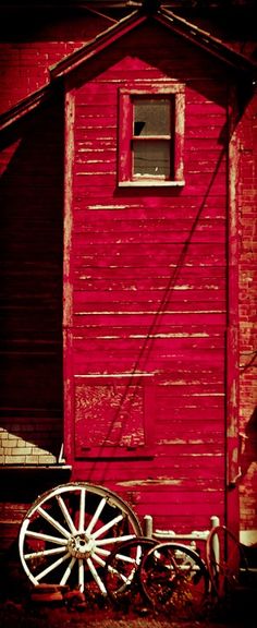 an old wooden wagon sitting in front of a red building with a window and door