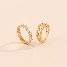 two gold rings sitting next to each other on a white surface, one has a diamond in the middle