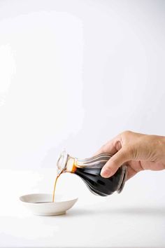 a person pouring sauce into a white bowl with a spoon in it on a white surface