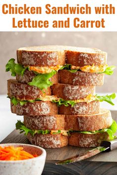 chicken sandwich with lettuce and carrots stacked on top of each other in front of a bowl