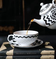 tea being poured into a black and white teacup on top of three book stacks