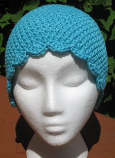 a white mannequin head wearing a blue crochet hat on top of a wooden table