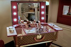 an old suitcase with makeup and other items in it sitting on a table next to a mirror