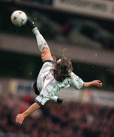 a soccer player is in mid air with the ball above his head as he kicks it