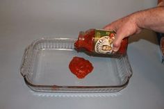 a person pouring ketchup into a glass dish