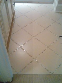 a bathroom floor with white tile and silver grouting on the ground, in front of a door