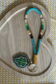 a wooden board with beads and a lanyard on the end that has a green leaf