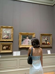 a woman looking at paintings on display in a museum