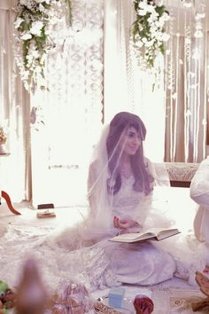 two women dressed in white sitting on the floor with their wedding dresses and veils pulled back