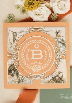 an orange and white card with the letter b on it next to some flowers in a vase