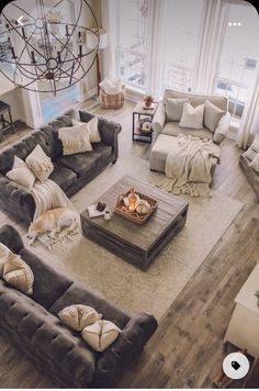 a living room filled with furniture and a chandelier hanging from the ceiling in front of two windows