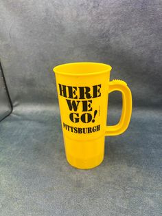 there is a yellow coffee cup that says here we go, pittsburgh on the side