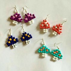 four different colored beads are hanging from earwires on a white surface, each with an individual's own design