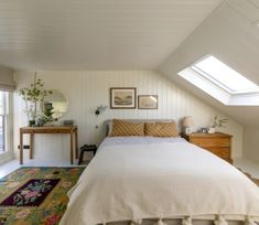 a bed sitting under a window in a bedroom next to a dresser and lamp on top of a rug