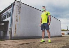 a man standing in front of a building wearing a yellow shirt and blue shorts with his hands on his hips