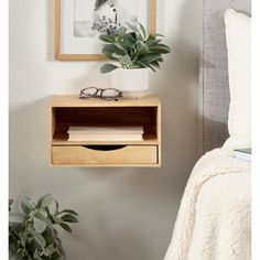 a bedroom with a bed, plant and eyeglasses on the nightstand next to it