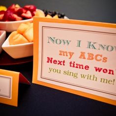 a table topped with bowls of fruit next to a sign that says now i know my abcs next time won't you sing with me