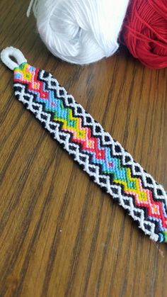 a colorful bracelet sitting on top of a wooden table next to balls of thread and yarn