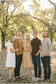 a group of people standing next to each other in front of trees and fallen leaves