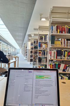 an open laptop computer sitting on top of a wooden table in front of a library filled with books