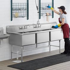 a woman cleaning a kitchen sink in front of two sinks with sprayers on the faucets