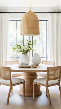 a dining room table with chairs and vases on it in front of a window