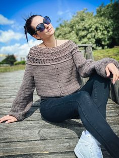 a woman sitting on a wooden bench wearing sunglasses and a crocheted sweater, with her eyes closed