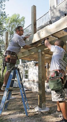 two men working on a wooden structure in the middle of a yard with ladders