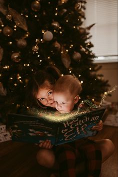 a young child reading a book next to a christmas tree