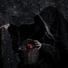 a creepy looking person holding a basket with an apple in it's hand and wearing a black cloak