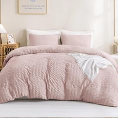 a bed with pink comforter and pillows in a white room next to a dresser