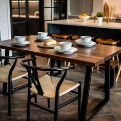 a wooden table topped with white plates and cups next to a kitchen island filled with cabinets