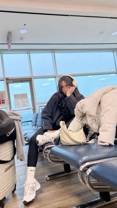 a woman sitting on top of an airport chair next to another person in the background