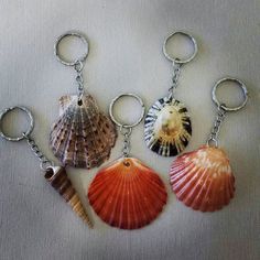 four seashells are shown in three different colors on a white surface, one is silver and the other is orange