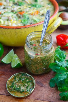 a bowl of soup with a spoon in it next to some limes and cilantro