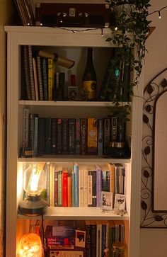 a bookshelf filled with lots of books next to a wall mounted clock and lamp