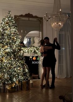 a man and woman dancing in front of a christmas tree