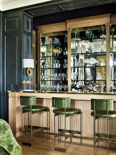 a bar with green chairs and shelves filled with glassware on the top shelf in front of it