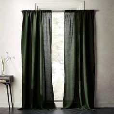 a green curtain hanging in front of a window next to a table with a plant on it